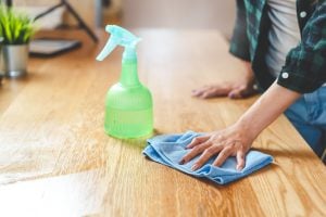 Close up woman cleaning a kitchen wooden worktop using cleanser spray and cloth.